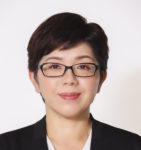 Japanese woman mid 30's dark short hair black rim glasses, black blazer bust portrait white shirt.